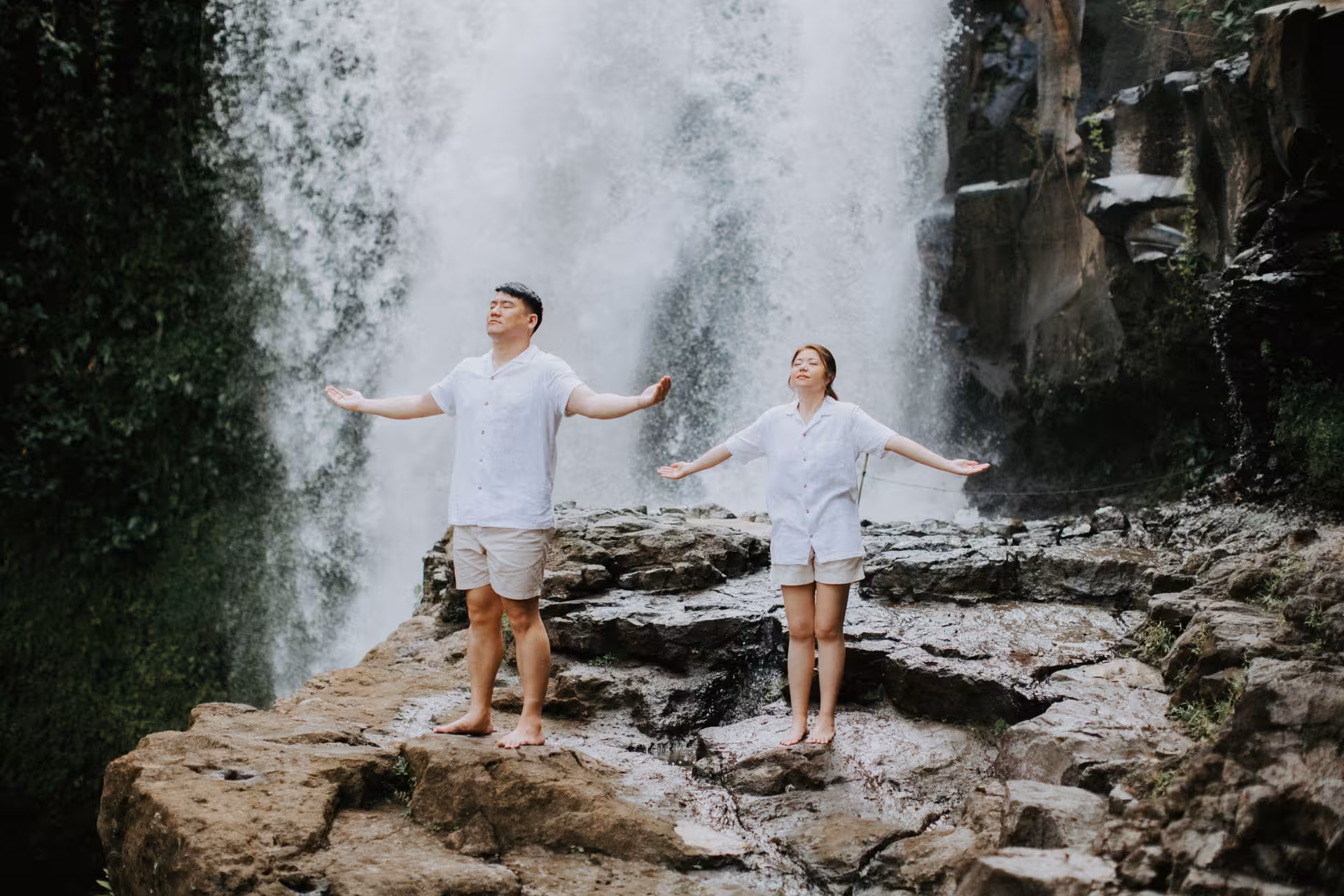 Couple embracing nature under a majestic waterfall in Bali during a private photoshoot experience.