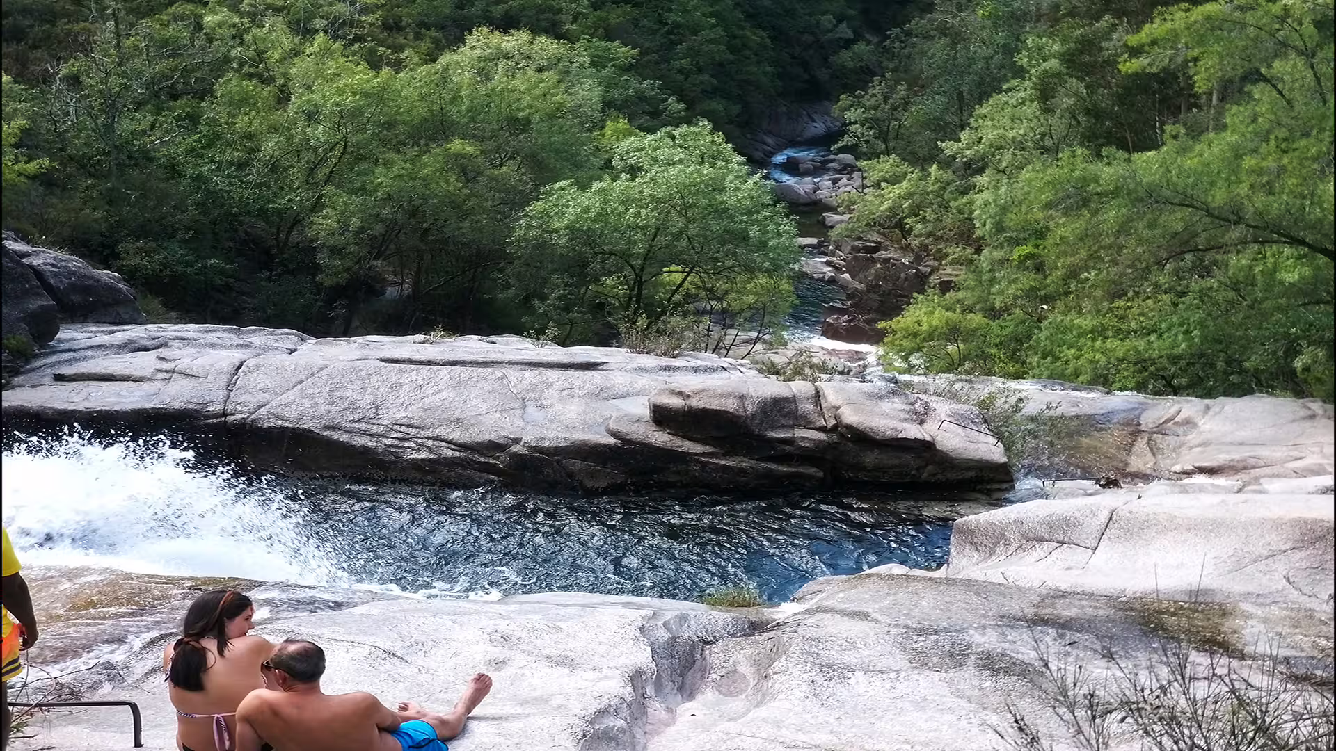 Couple enjoys stunning waterfall view at Peneda-Gerês National Park, highlighting lush greenery and serene nature experience.