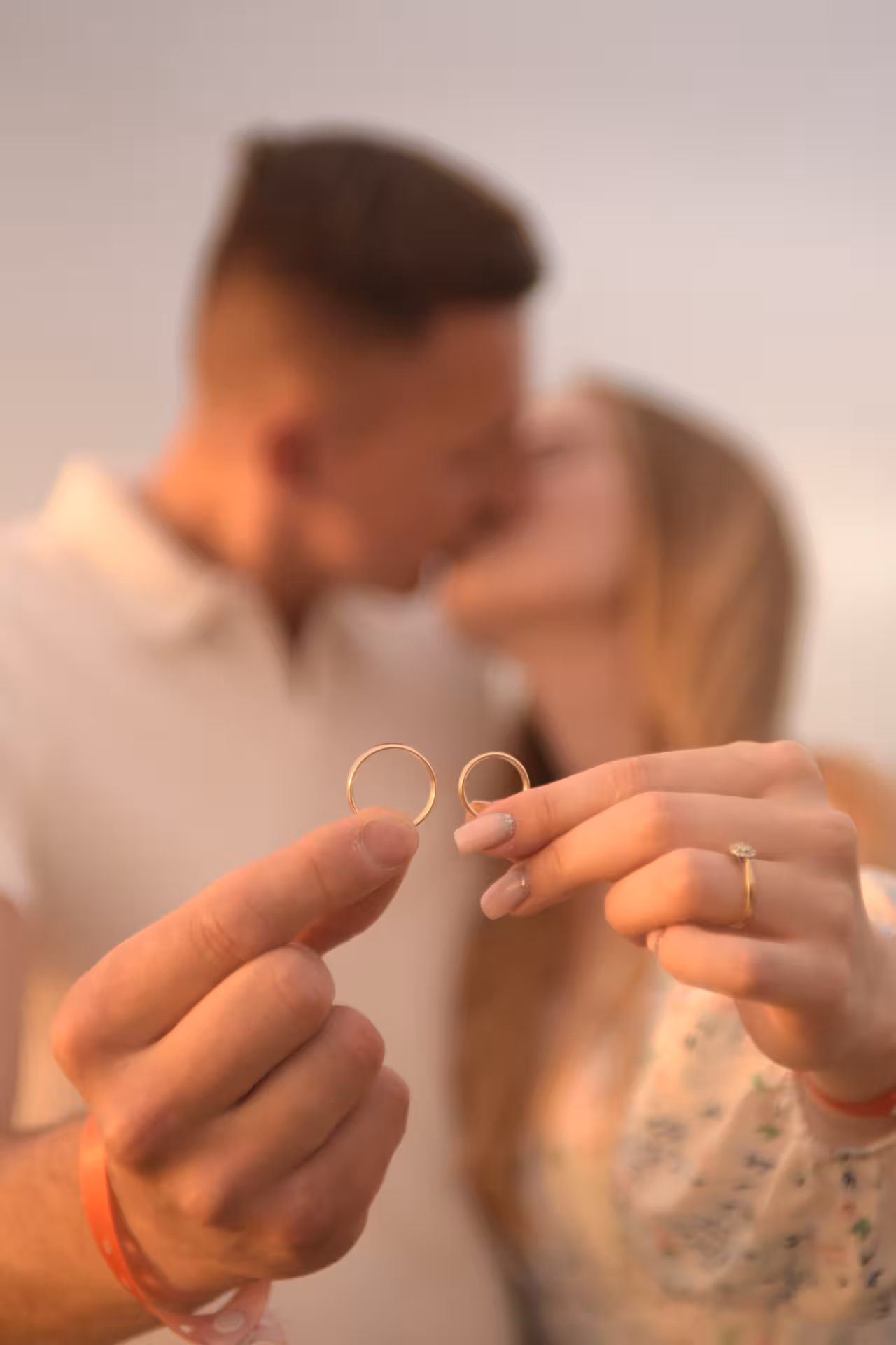 Couple holding wedding rings in focus, sharing a kiss in the background during a surprise proposal at Heraklion Port.