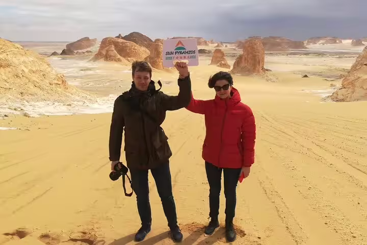 Couple at Egypt’s White Desert rock formations on a private day tour from Bahariya Oasis, holding tour sign