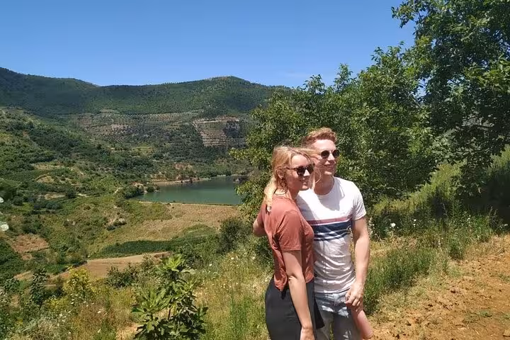 A couple embracing with a picturesque view of Berat's green hills and a serene lake.