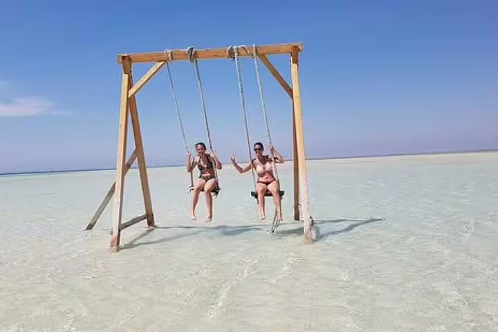 Couple on wooden sea swing in shallow turquoise water at Orange Bay Island, VIP boat trip Hurghada