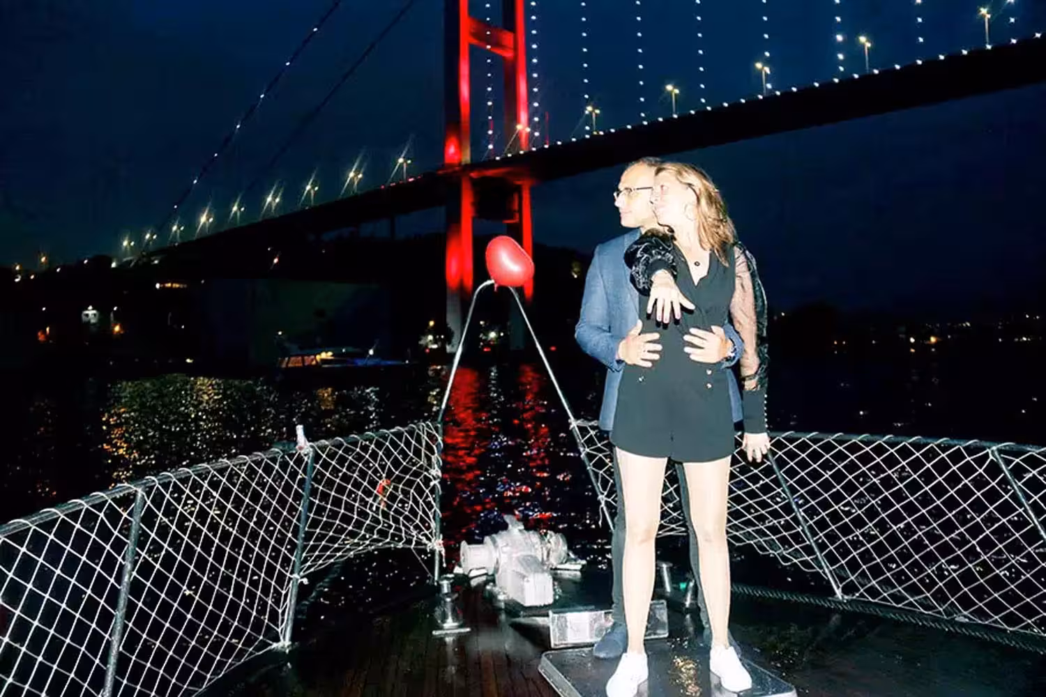 Couple hugging on a private yacht at night beneath the illuminated Bosphorus Bridge, romantic proposal cruise