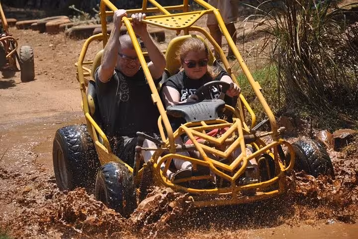 Couple driving a yellow off-road buggy through muddy water on Great Threesome rafting buggy zipline tour