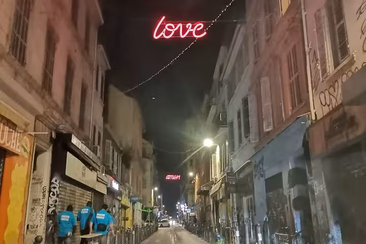 Night stroll in Marseille’s Cours Julien district with neon love sign above lively street art-lined lane