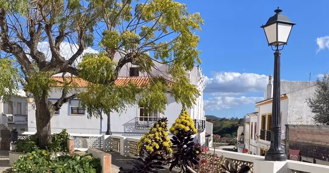 Sunny whitewashed village square with leafy trees and traditional houses on The Crafts & Mountains Journey in rural hills