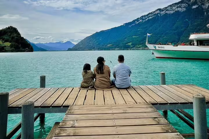 Family enjoys serene views from a dock on Lake Brienz, Switzerland, with a boat nearby, part of a Crash Landing on You tour.
