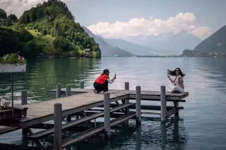Tourists capture memories on a scenic dock over a Swiss lake, surrounded by lush mountains, on a Crash Landing on You tour.