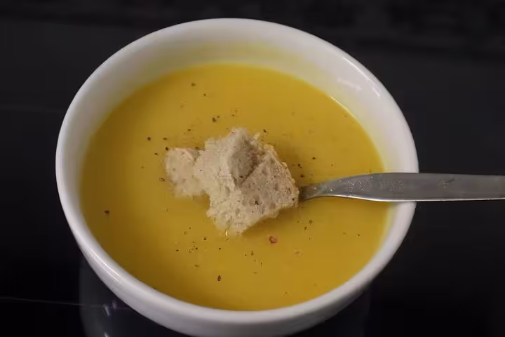 Creamy pumpkin soup garnished with a piece of rustic bread in a white bowl, perfect for a cozy Portuguese terrace dining experience.