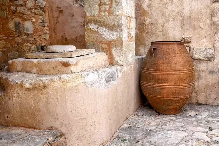Ancient stone mill and large clay pot in a rustic Cretan village setting, showcasing traditional Apokoronas architecture.