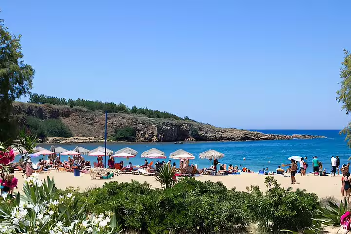Sunny Crete beach with umbrellas and tourists enjoying the pristine sand and blue sea, perfect for a relaxing day.