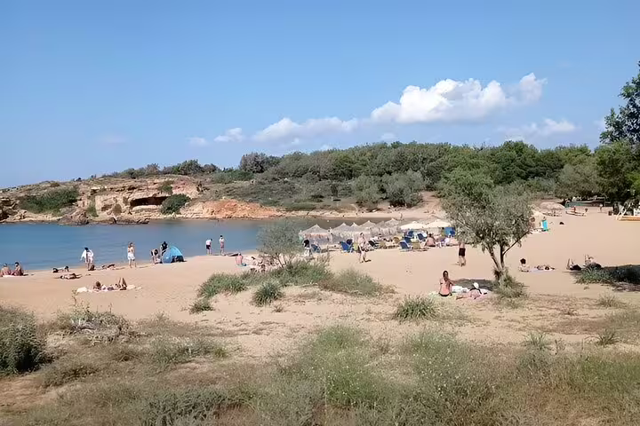Relaxing Crete beach scene with sunbathers, umbrellas, and lush greenery against a clear sky backdrop.