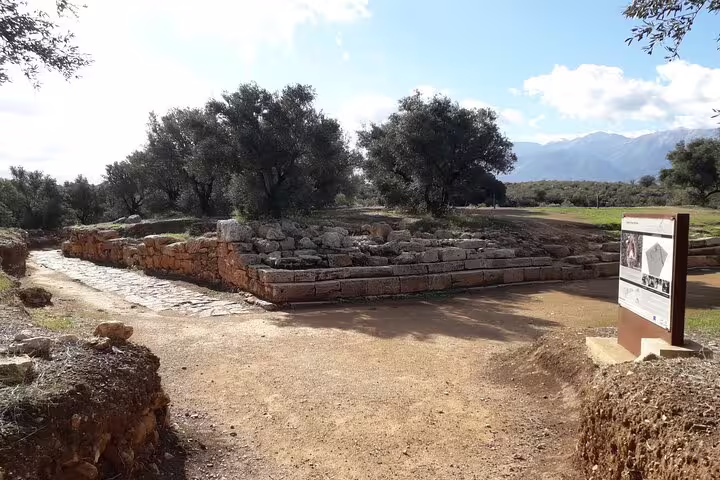 Ancient stone ruins surrounded by olive trees in the serene Crete countryside under a clear blue sky.
