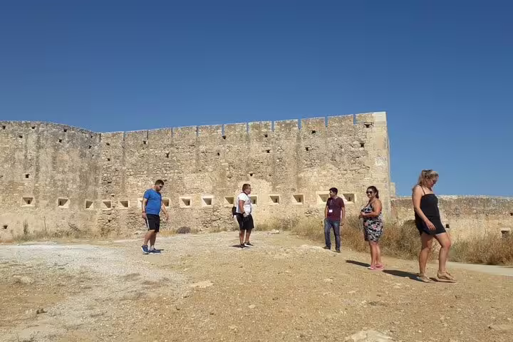 Visitors exploring the historic walls of a stone fortress on a sunny day in Crete's countryside.