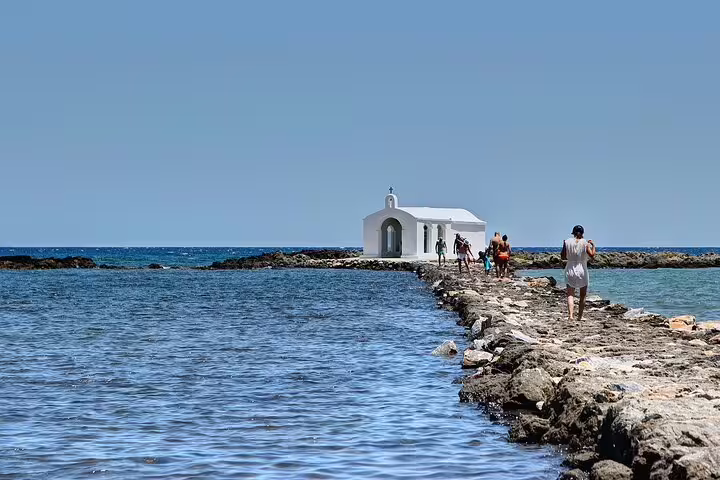 Visitors walking along a rocky path to a picturesque white chapel on the sea during a Crete countryside private tour.