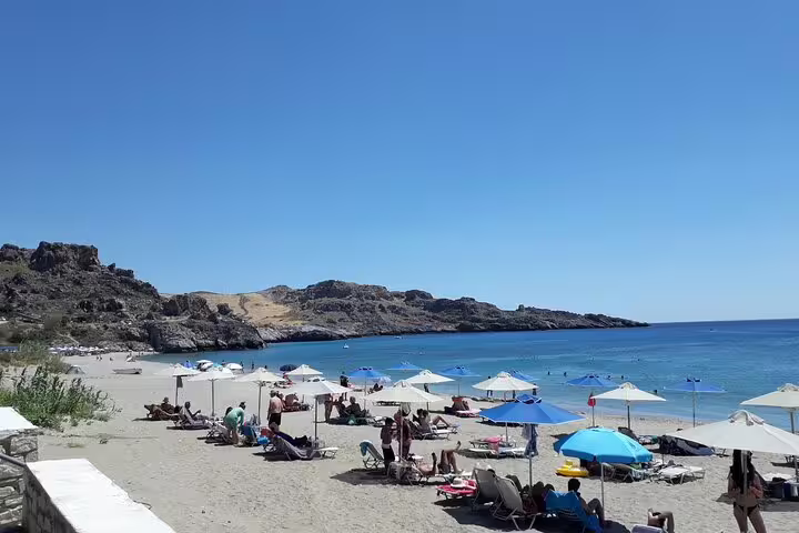 Relaxing beach scene on Crete's south coast with sunbathers and umbrellas set against a stunning rocky backdrop.