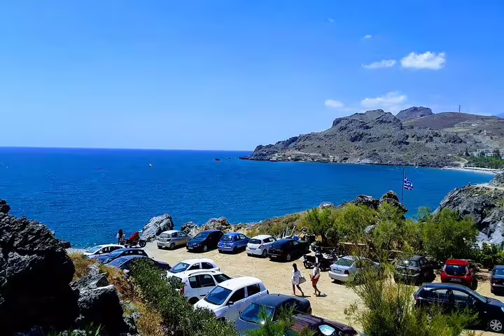 Scenic view of Crete's south coast with cars parked near the azure sea on a sunny day during a private tour.