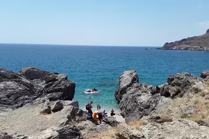 Visitors enjoying a serene rocky beach with clear blue waters on Crete's south coast, perfect for exploration.