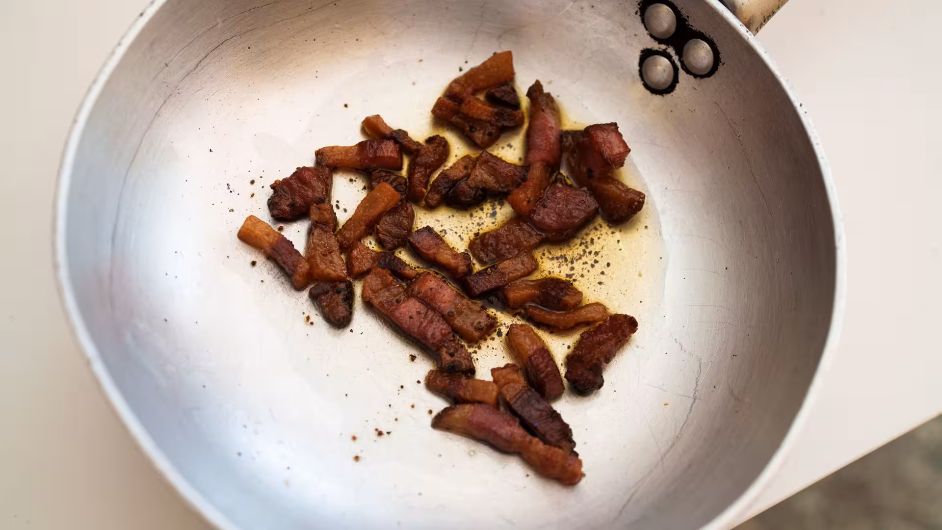 Crispy pancetta sizzling in a pan, a key ingredient in authentic Olbia pasta carbonara cooking class.