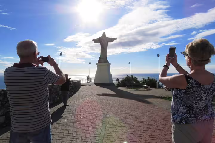 Tourists capture photos of the Cristo Rei statue against a bright sky during a guided 4-hour tour from Funchal, Madeira.
