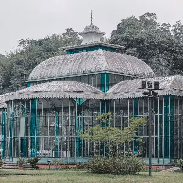 The iconic glass and iron structure of the Crystal Palace in Petrópolis, surrounded by lush greenery.