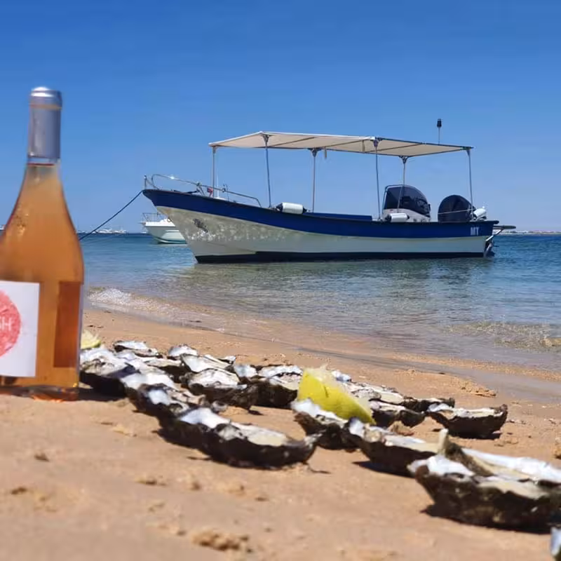 Sandy beach on Culatra Island with a boat, oysters, and wine, perfect for a relaxing getaway in the Algarve region.