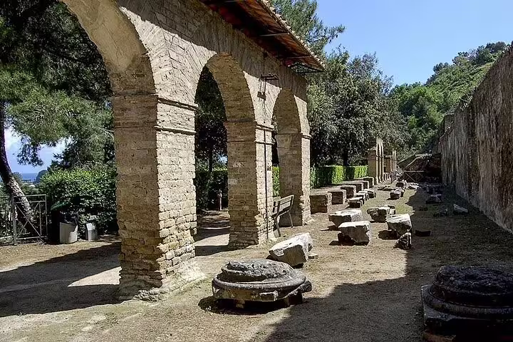 Arched walkway and stone remains of the Cuma archaeological site surrounded by greenery on a private tour from Naples
