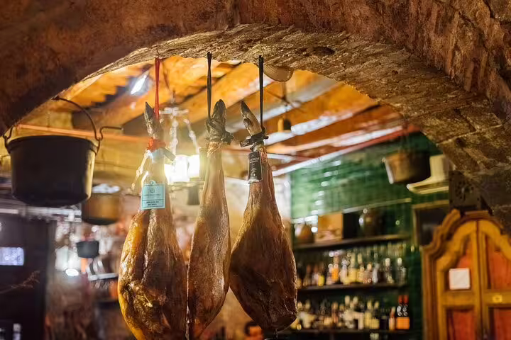 Hanging cured hams in a traditional Spanish tavern, ideal setting for a tapas and wine walking tour.