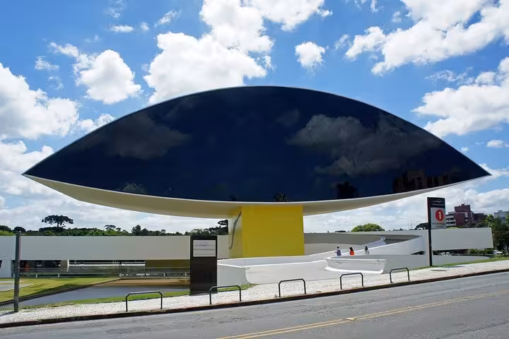 Contemporary art museum with eye-shaped design against blue sky on Curitiba city tour.