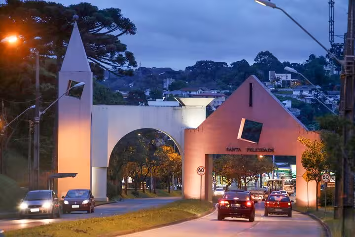 Evening view of the illuminated entrance to Curitiba's Santa Felicidade district, showcasing iconic architecture and vibrant street life.