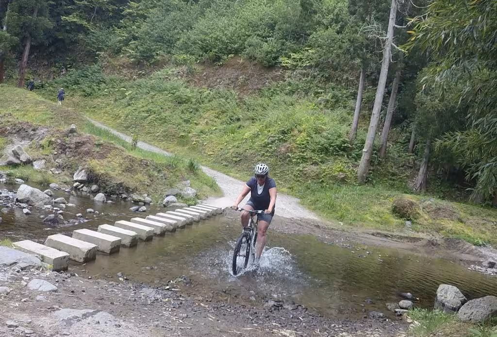 Cyclist splashing through a shallow stream on the Furnas half-day bike tour, Azores off-road trail