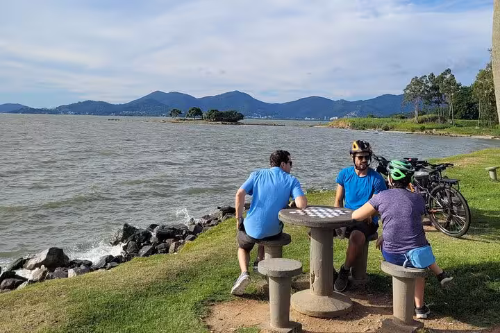 Cyclists enjoy a scenic break by the lake during a bike tour in Florianopolis, surrounded by mountains and nature.