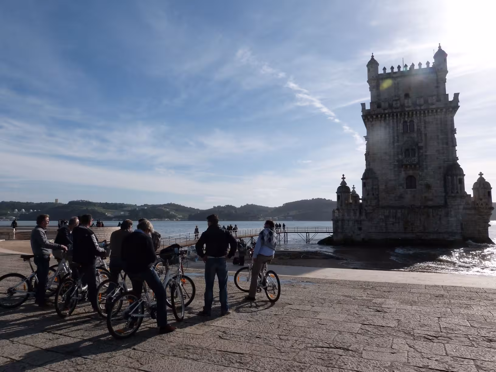 Cyclists pause at the iconic riverside tower during the River Light Bike Tour in Lisbon, enjoying scenic views.