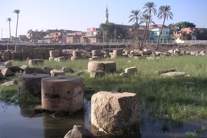 Memphis archaeological ruins with stone blocks, palm trees and village skyline on Dahshur Pyramid and Memphis tour