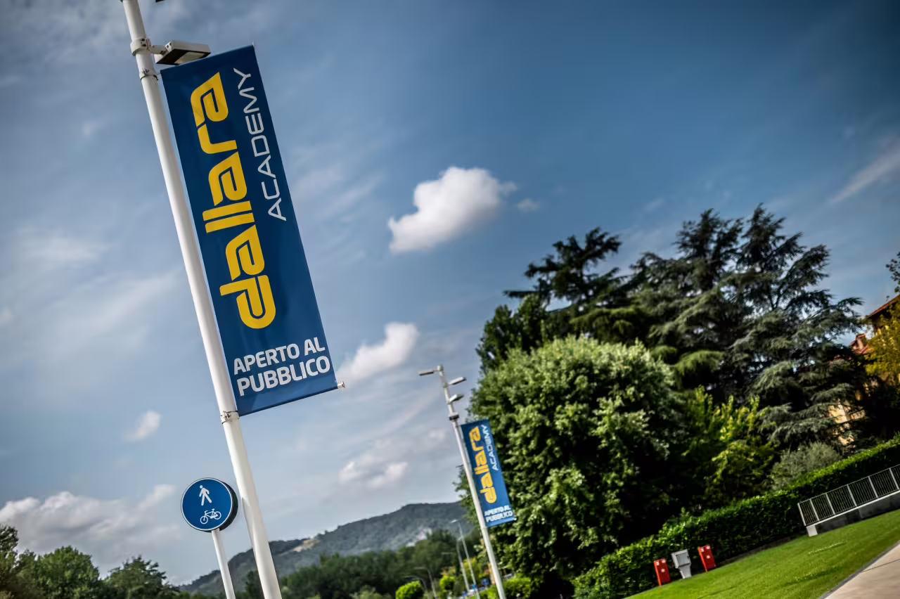 Dallara Academy public signage against a blue sky, inviting visitors to explore motorsport excellence in Parma.