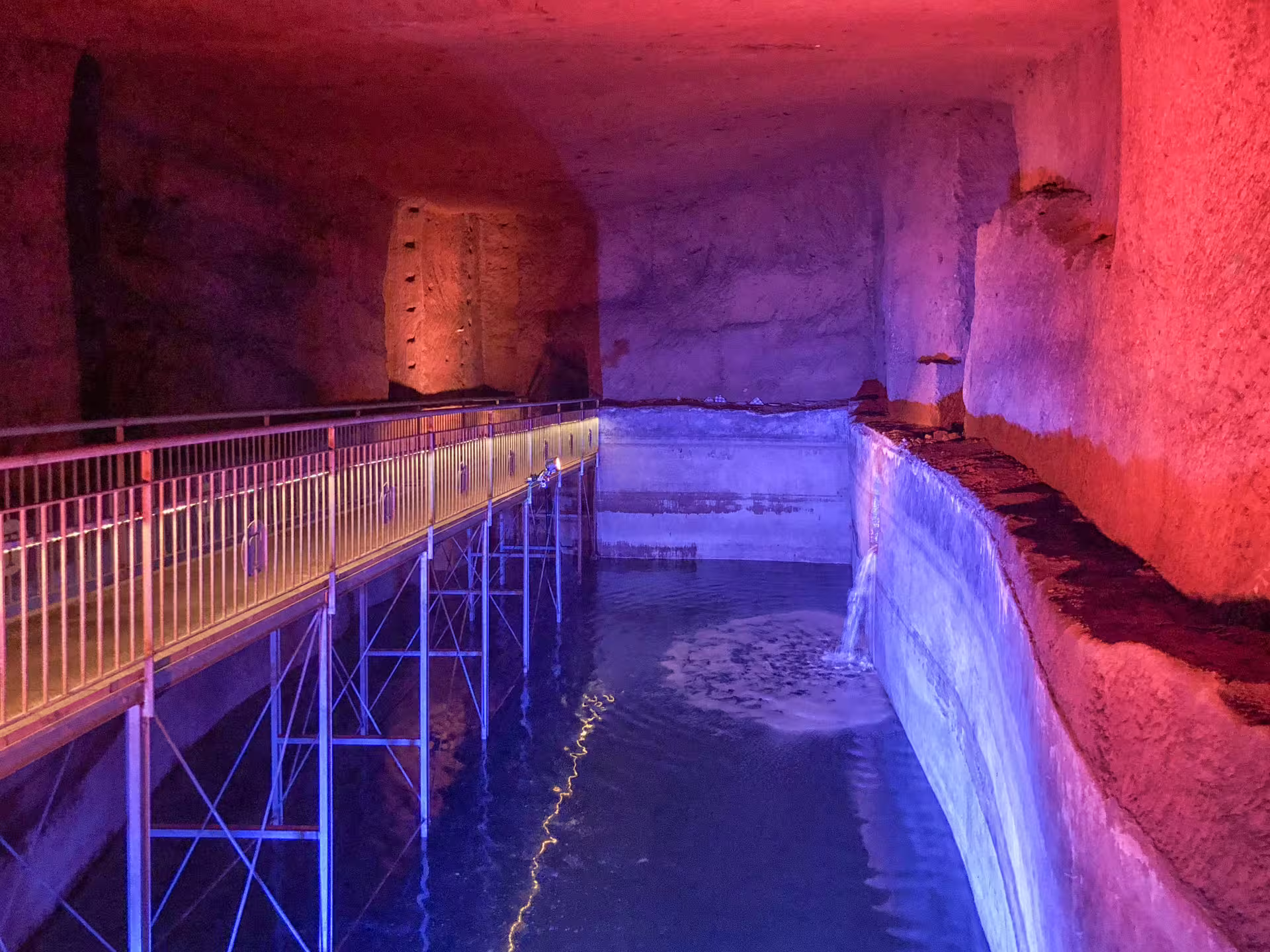 Colorful illuminated underground water cavern and walkway on the L'Inferno di Dante al Decumano Sommerso Naples tour