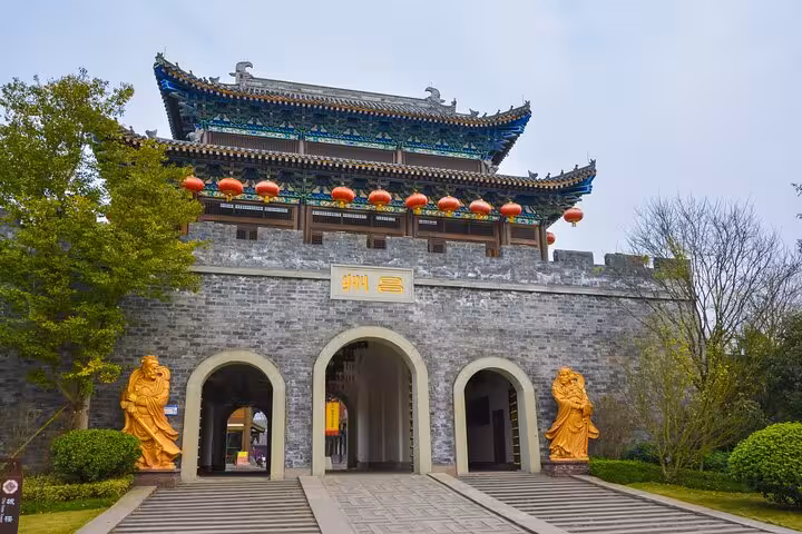 Ancient Chinese gate adorned with red lanterns and golden statues at Dazu Rock Carvings entrance in Chongqing.