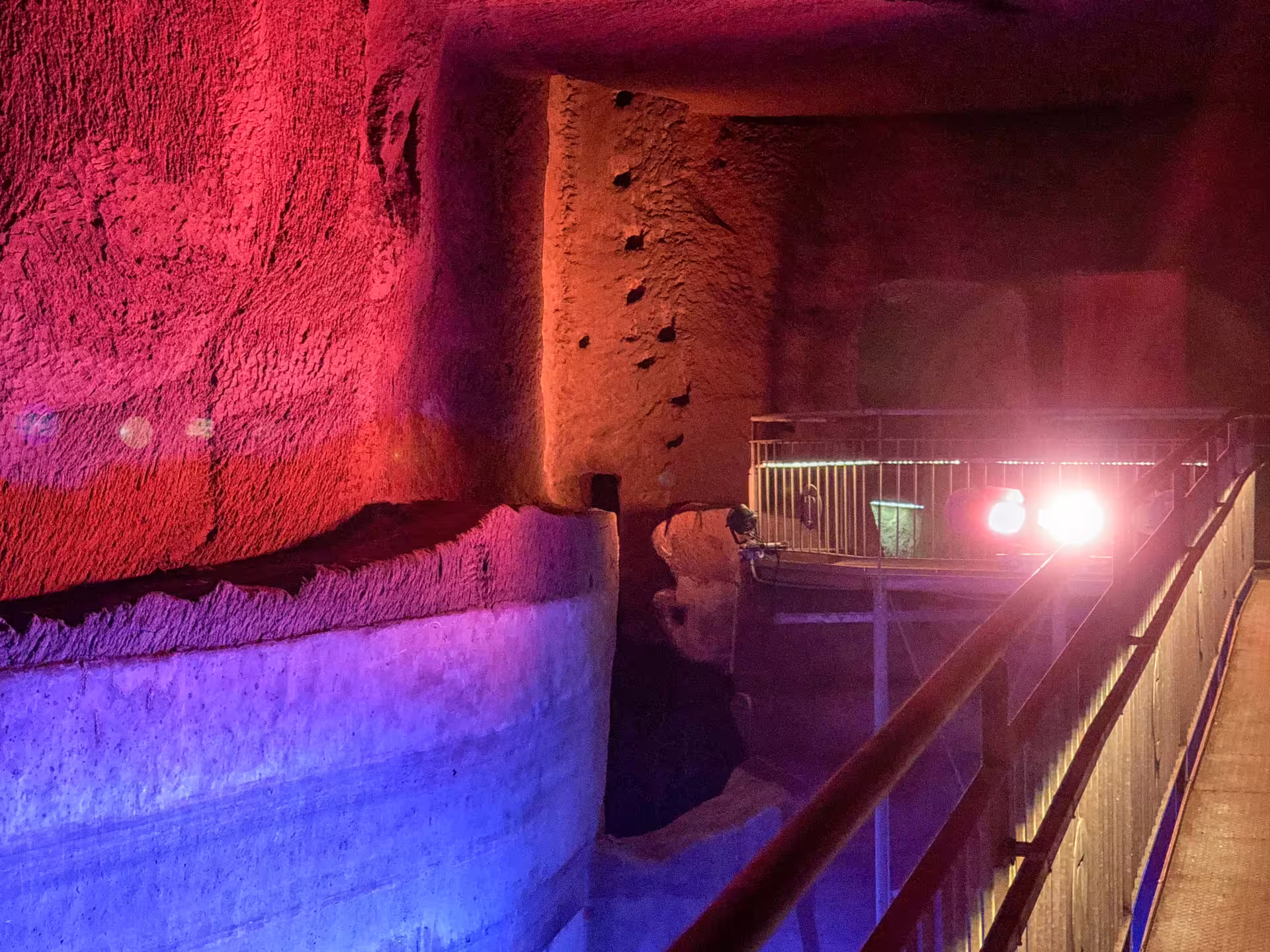 Colorful lights highlight the carved rock walls and elevated walkway inside the Decumano Sommerso tour at Lapis Museum Naples