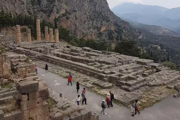 Small group walking through Delphi archaeological site ruins and temple columns on a guided day tour from Athens