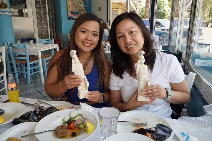Guests enjoy Greek dinner and hold souvenir figurines, Delphi and Meteora private day trip from Athens