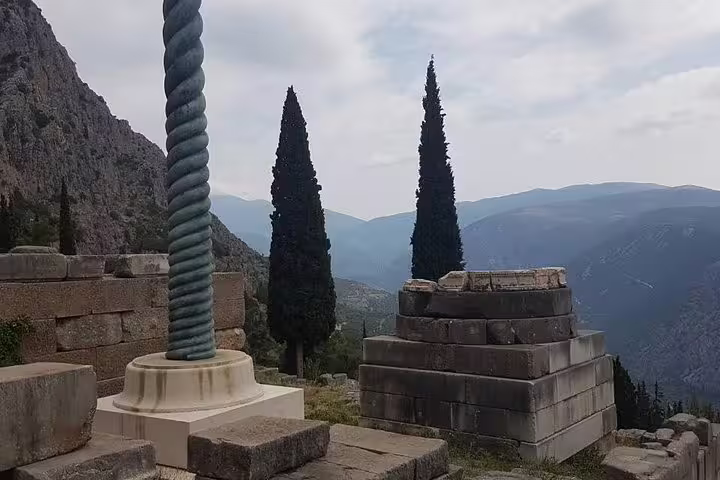 Delphi sanctuary viewpoint with ancient stone base and cypress trees, part of a guided small group day tour from Athens