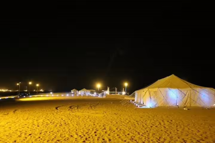 Night view of a desert camp with glowing tents for a BBQ meal under the stars.