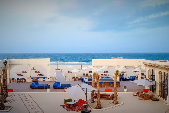 Luxurious desert camp with oceanfront view, featuring elegant seating areas and white parasols on a sunny day.
