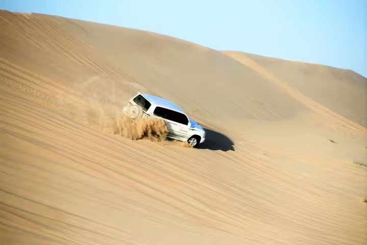 4x4 vehicle navigating steep sandy dune during thrilling desert safari adventure.