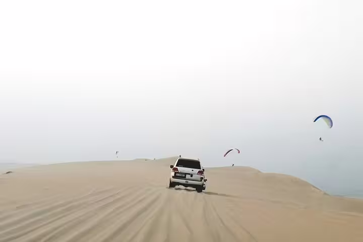 4x4 vehicle navigating sand dunes with parasailers in the sky during a desert safari adventure.