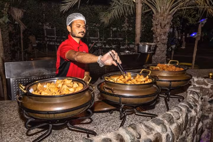 Hot buffet dinner at Ras Al Khaimah desert safari camp, chef serving Arabic snacks under palm trees