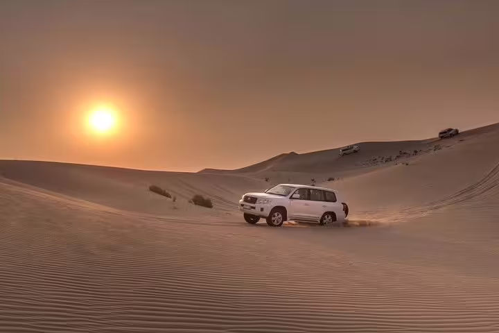 Desert safari at sunset with a 4x4 vehicle navigating the golden dunes.