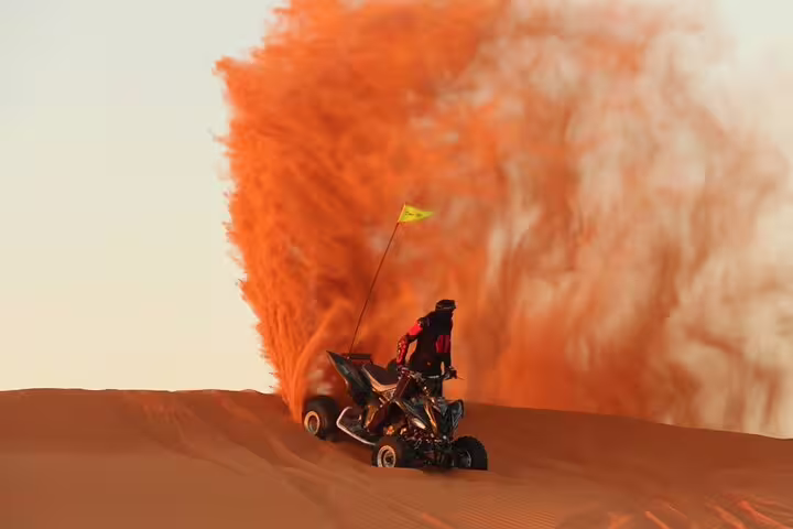 Rider on a quad bike kicks up vibrant red sand on a thrilling desert safari adventure across the expansive dunes.