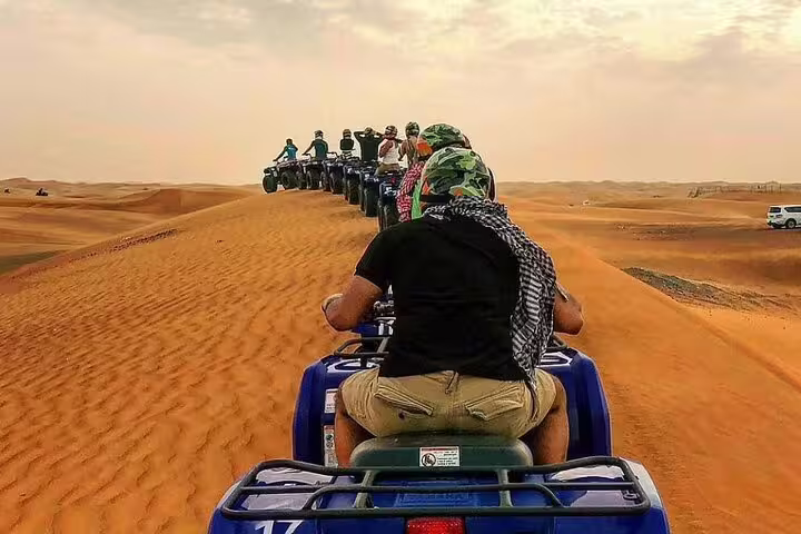 Adventurers ride quad bikes over stunning red dunes during an exhilarating desert safari experience under a vast, cloudy sky.