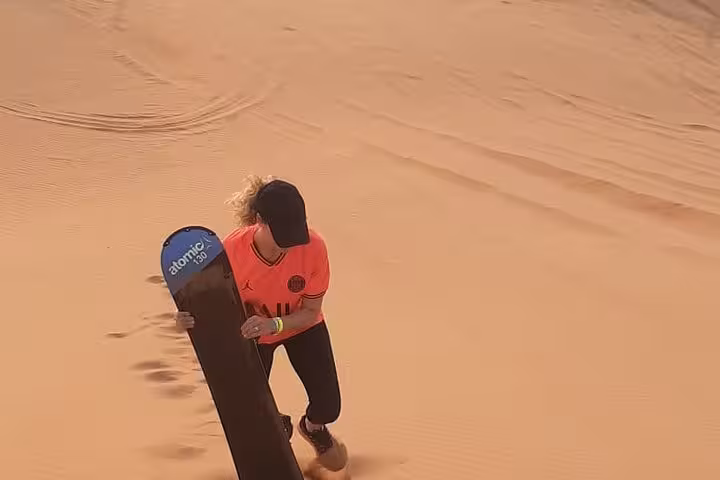 Guest hiking up a sand dune with sandboard on a private morning desert safari, before flamingo bird watching